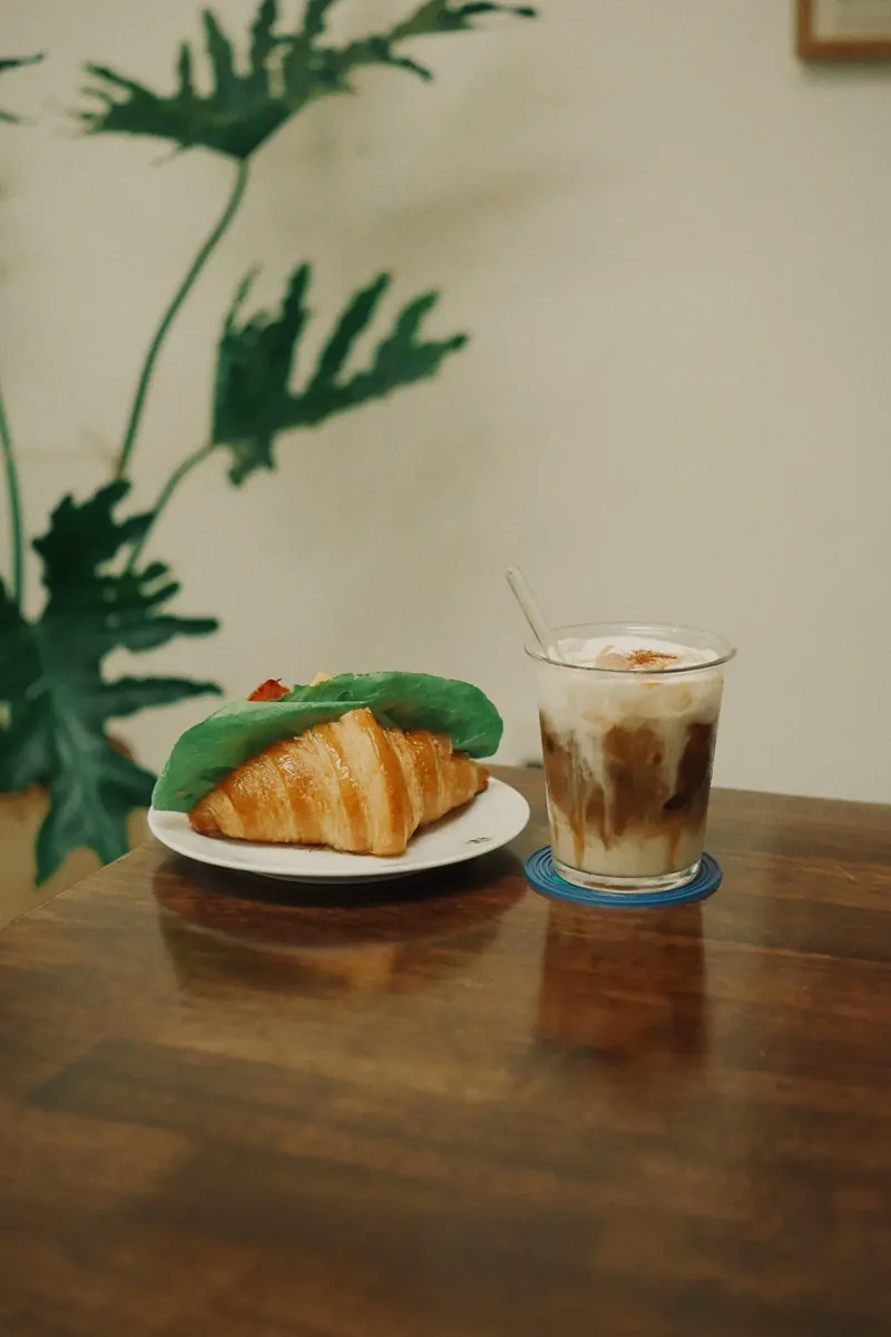 Croissant mentega di samping segelas es kopi
