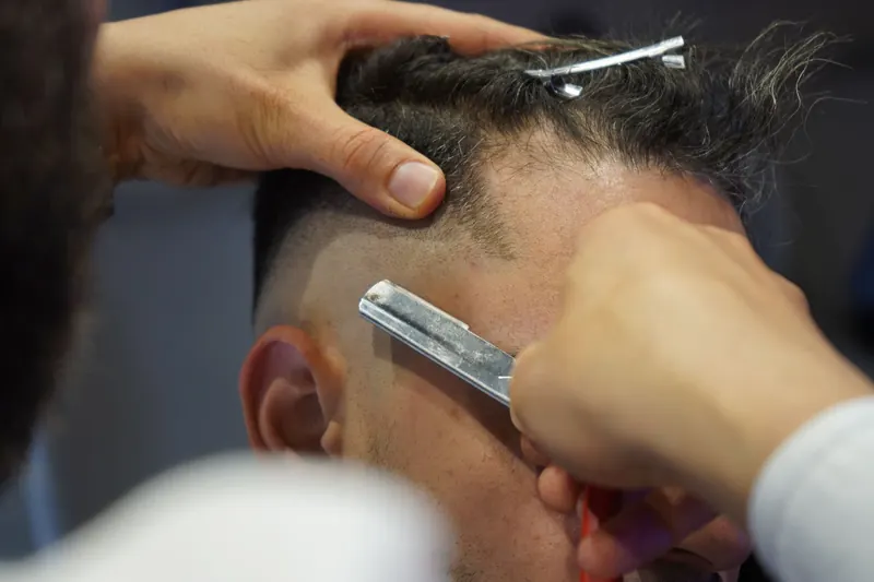 Tukang cukur merapikan rambut dengan mesin