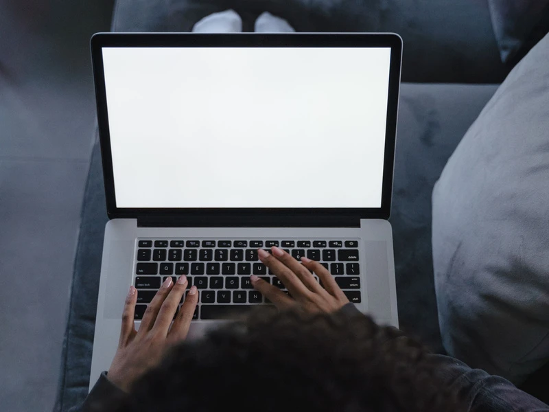 Seseorang dari samping mengetik di laptop dengan layar putih