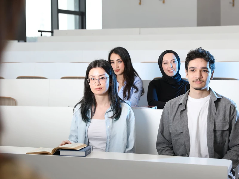 Empat orang duduk di ruang kuliah, masing-masing di depan laptop