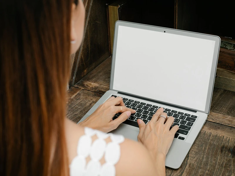 Tangan di atas laptop dengan layar putih, dilihat dari atas