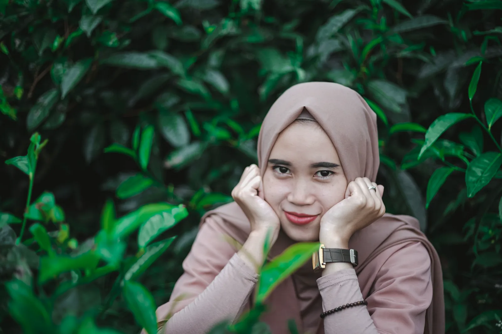 Perempuan berkerudung merah muda tersenyum di taman
