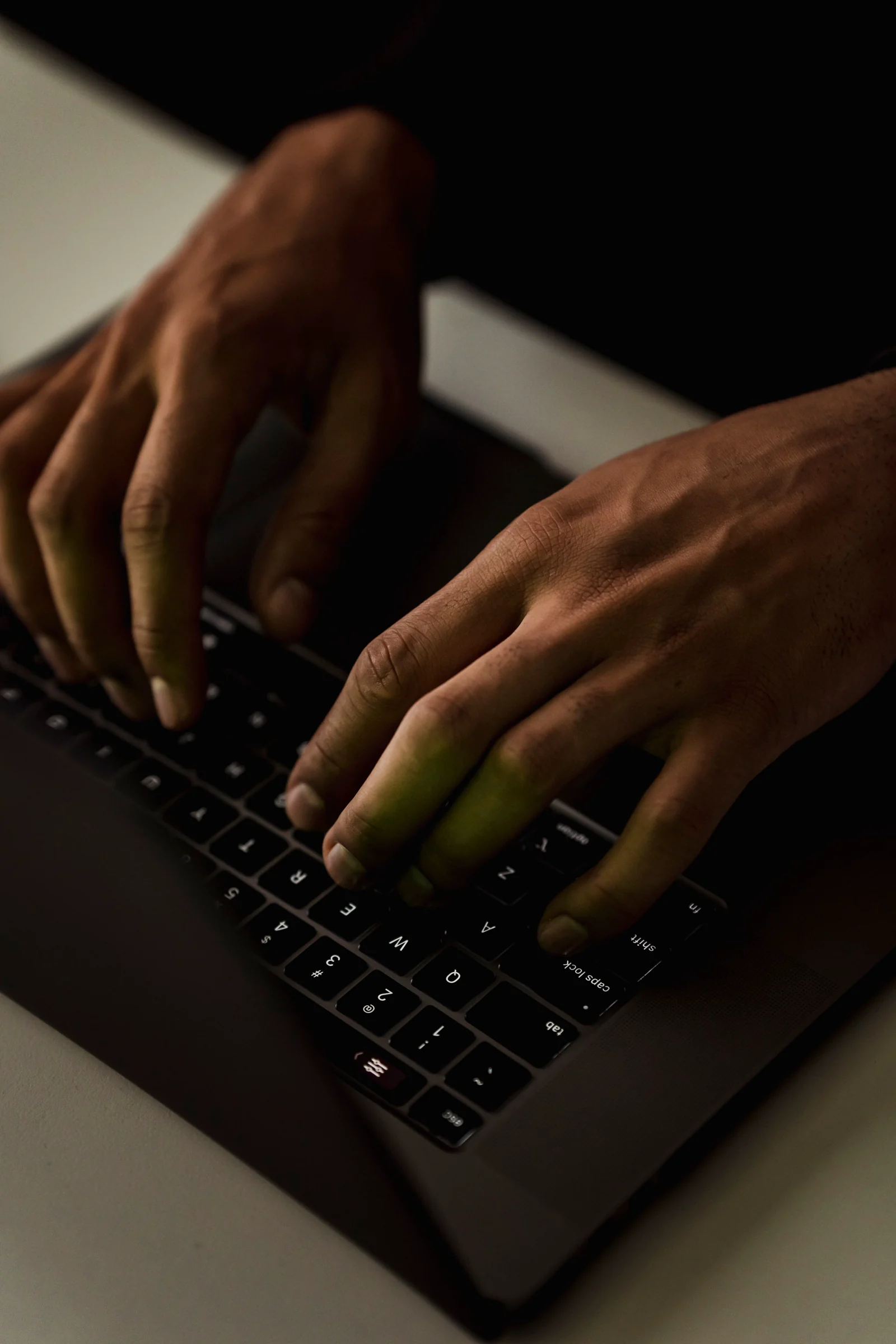 Tangan di atas papan ketik laptop, layar di luar bingkai