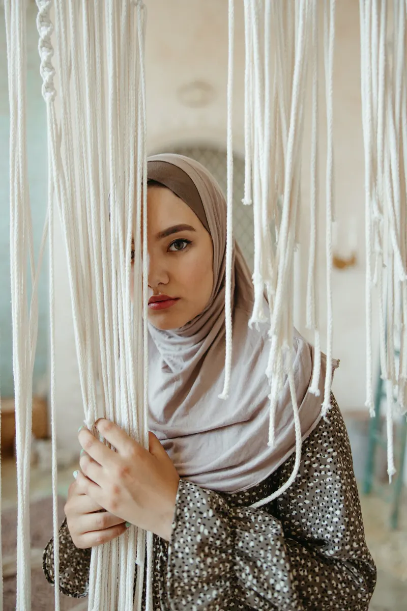 Model berhijab berdiri di antara gulungan benang